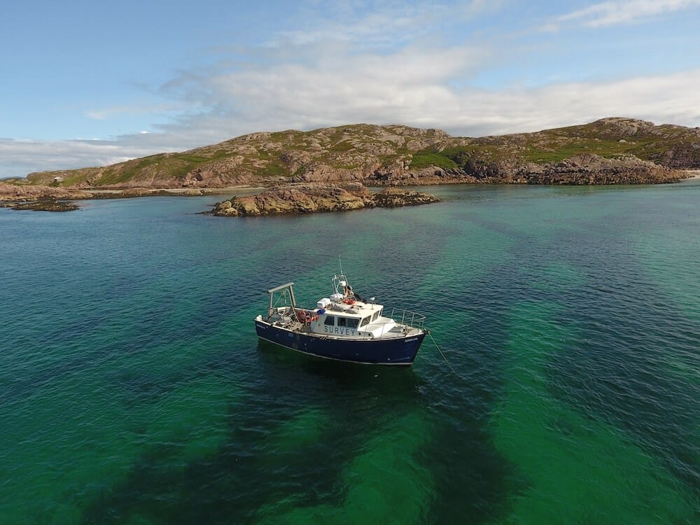 Small survey boat - The Seren Las on a green and blue sea near a rocky shore