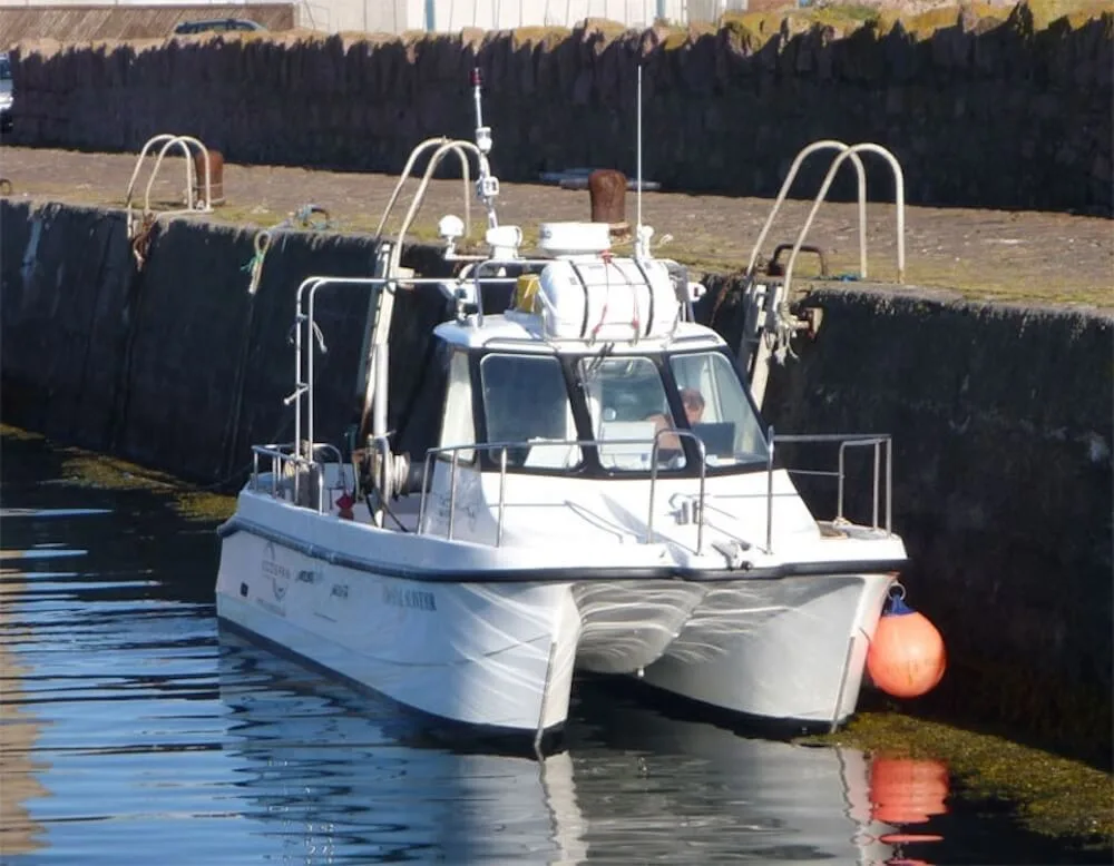 Small catamaran (Coastal Surveyor) moored on a harbour wall