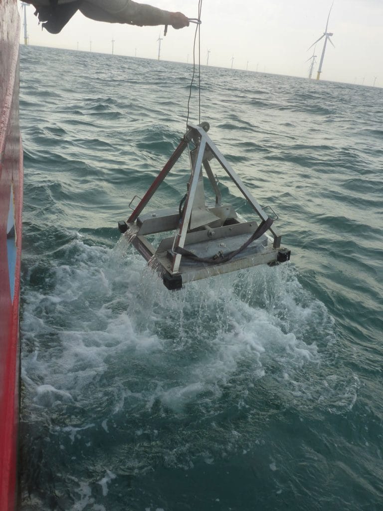 Picture of a grab sample being retrieved from the sea with a wind farm in the background