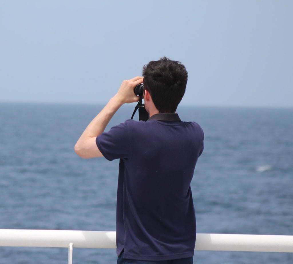 Picture of a male marine mammal observer looking out to sea through binoculars