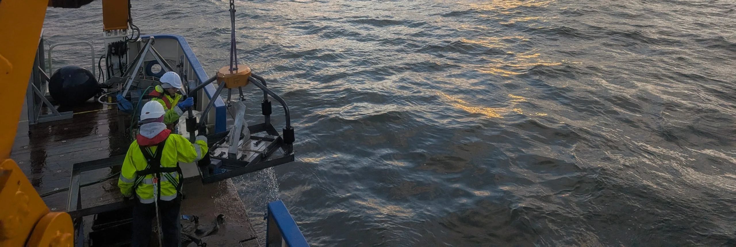 Picture of survey crew deploying a grab over the side of a vessel at sea